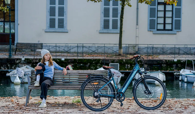 Eine Frau sitzt auf einer Parkbank und betrachtet ein Fiido C11pro Elektrofahrrad