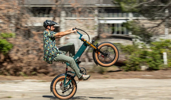 Ein Fahrer macht auf einem Fiido M1 Pro Fat-Tire-E-Bike einen Wheelie und präsentiert dabei den kompakten Klapprahmen, die breiten Reifen und die Vorderradfederung auf einer städtischen Straße.