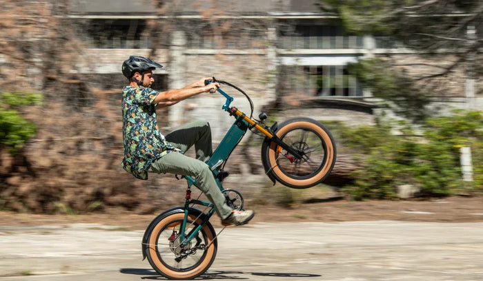 Ein Fahrer macht auf einem Fiido M1 Pro Fat-Tire-E-Bike einen Wheelie und präsentiert dabei den kompakten Klapprahmen, die breiten Reifen und die Vorderradfederung auf einer städtischen Straße.