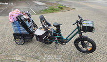 Ein Fiido T2 Cargo-E-Bike ist voll beladen mit einem Kindersitz, seitlichen Packtaschen, einer vorderen Transportbox und einem schwer beladenen Fahrradanhänger zu sehen.
