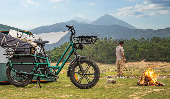 Fiido T2 E-Lastenrad mit Campingausrüstung beladen auf einem Bergcampingplatz neben einem Zelt und einem Lagerfeuer